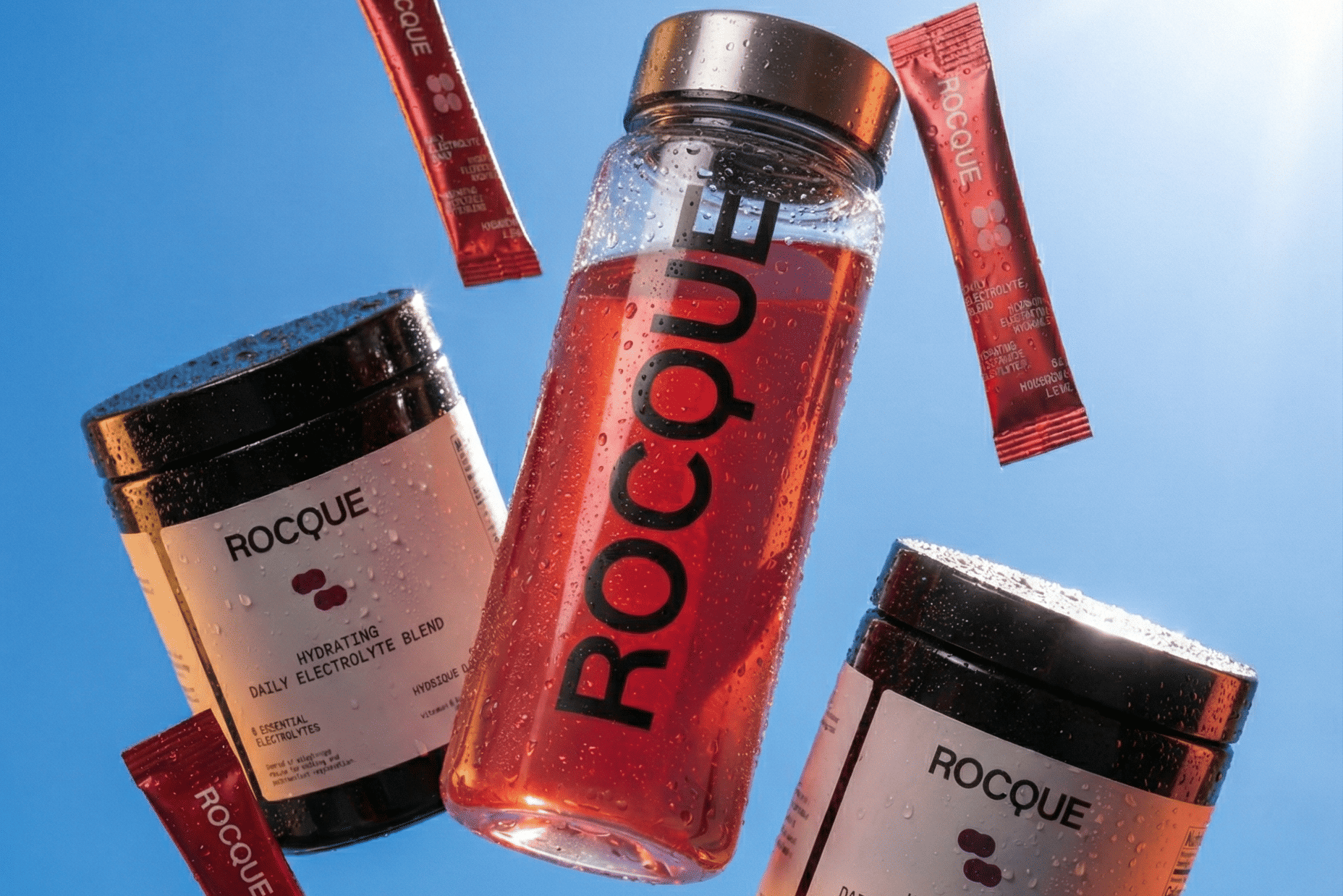 ROCQUE electrolytes including a bottle, containers, and sachets dropping on a blue sky background