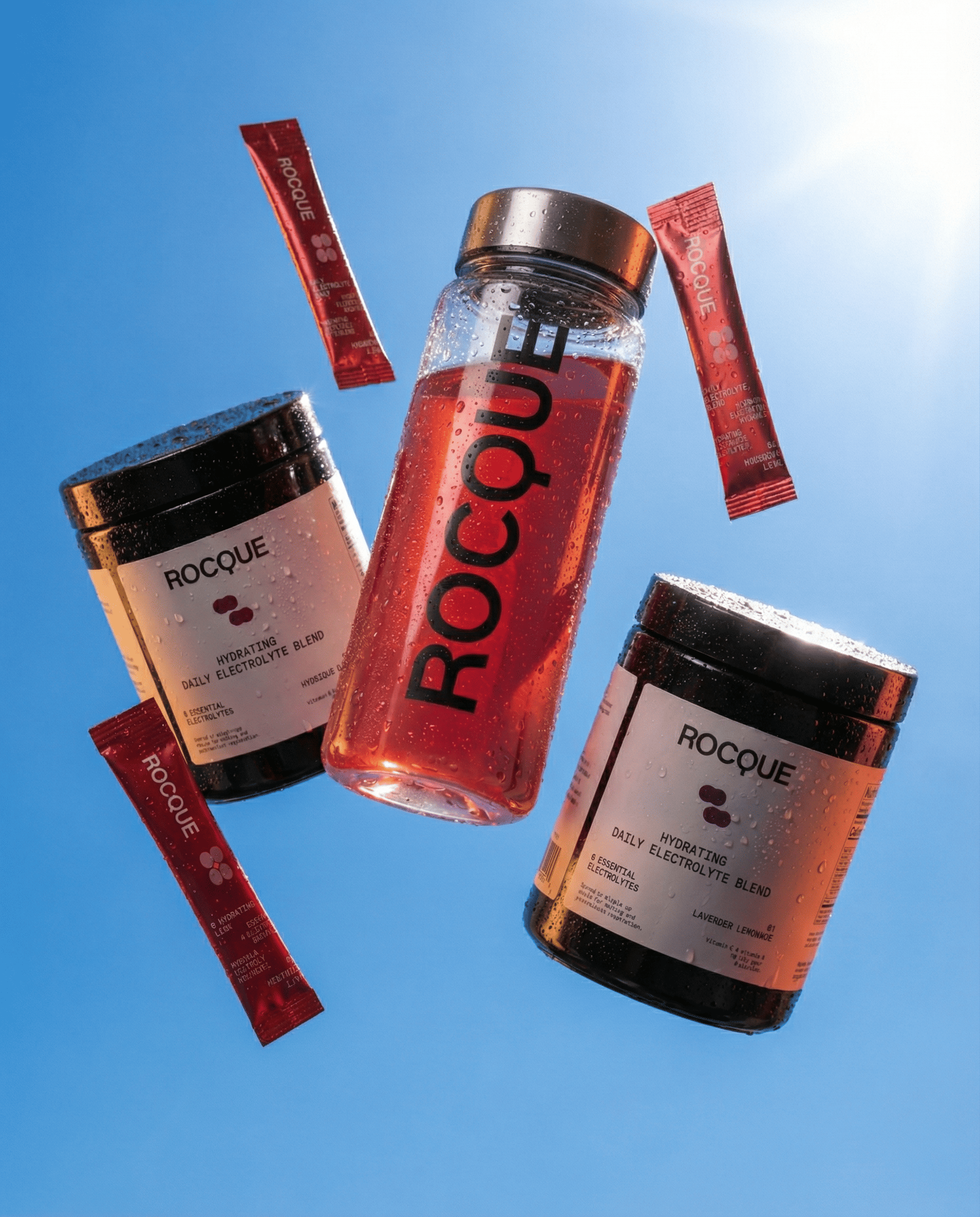 ROCQUE products including a bottle, containers, and sachets dropping from a blue sky background