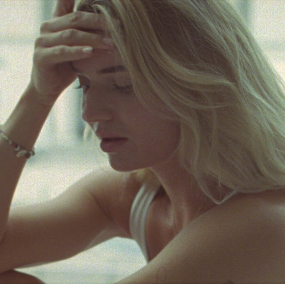 Woman with blonde hair holding her head in a blurred outdoor setting